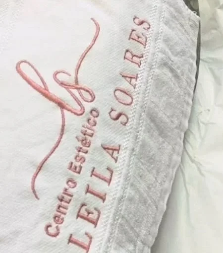 Toalha branca com o monograma ls e o nome Centro Estético Leila Soares bordados em linha rosé